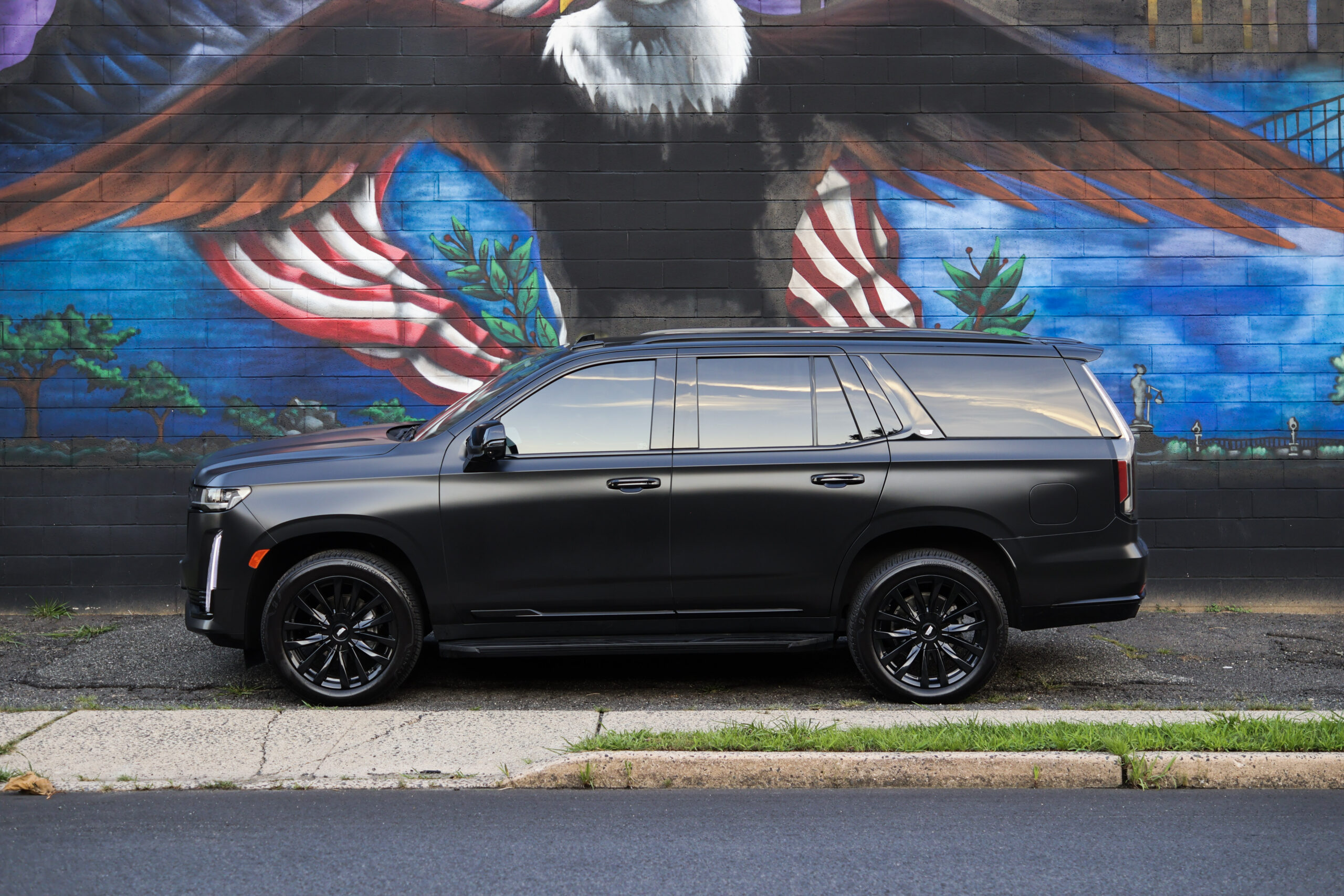 Black 2023 Cadillac Escalade side profile in front of a mural
