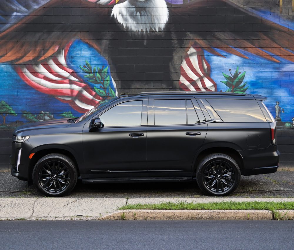 Black 2023 Cadillac Escalade side profile in front of a mural