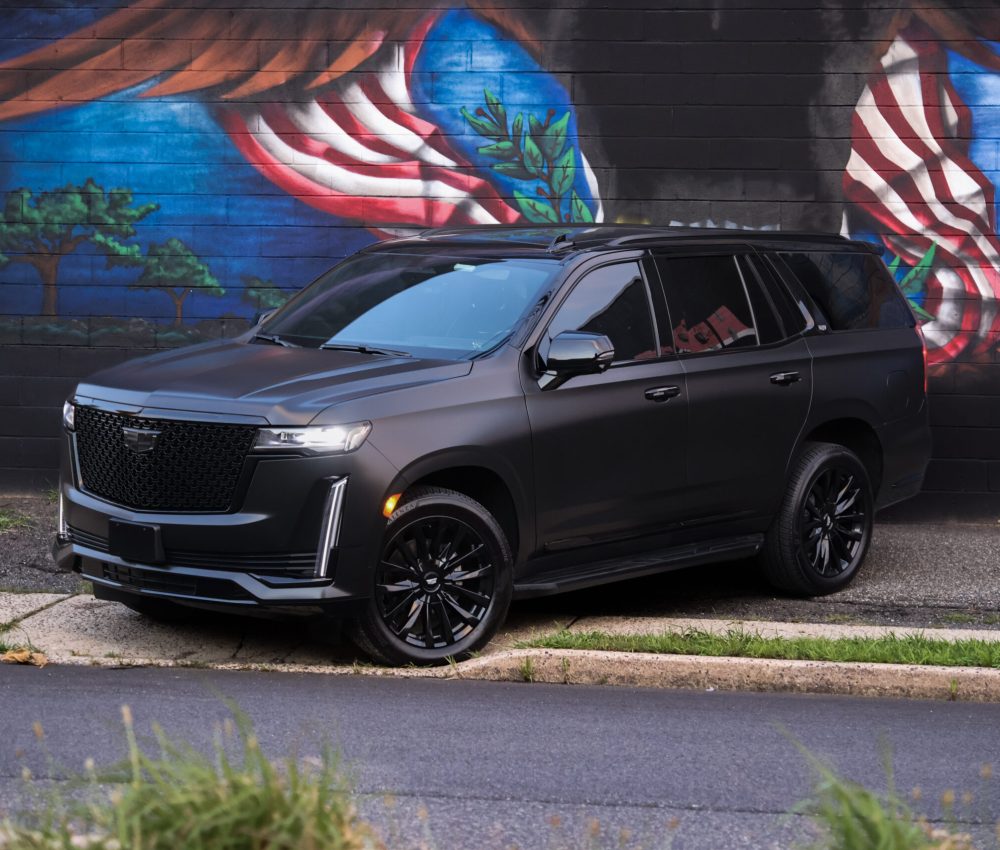Black 2023 Cadillac Escalade from the front left in front of a mural